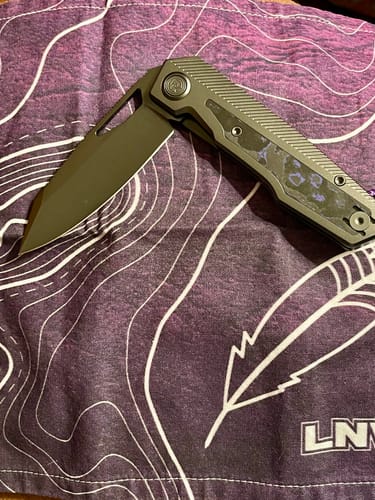 Customer's Divo Knives Saloon knife with a dark blade and Camo Carbon handle, shown partially open on a purple cloth.