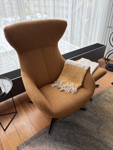 Beoordelaar toont de beige SALME plaid met franjes, losjes gedrapeerd over een fauteuil.