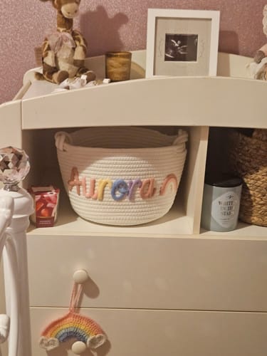 Customer's woven basket personalized with the name 'Aurora' in colorful letters, sitting on a nursery shelf.