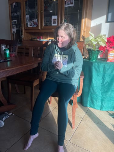 Customer seated indoors wearing the deep green Piper Pocket Petite leggings with a hoodie.