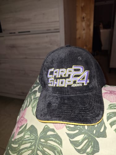 Klant toont de zwarte fluwelen Carpshop24-pet met het logo op de voorkant.
