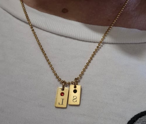 Close-up of a reviewer wearing the gold Birthstone Tag necklace with two personalized initial charms.