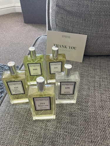 Reviewer's 'Inspired By Snow Angel - 178' perfume bottle displayed with four other fragrances on a grey sofa.