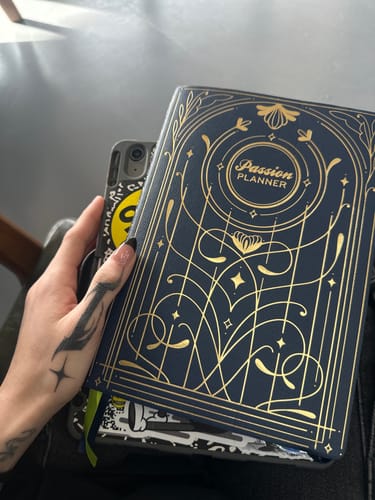 Customer holding the Cosmic Charm 2026 Weekly Planner, showing the dark purple cover with its gold foil design.