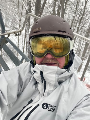 Reviewer on a snowy ski lift wearing the white Picture Goods Jacket.