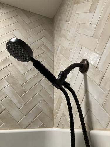 Reviewer's black Shark Skin Grip installed on a handheld shower head in a tiled shower.