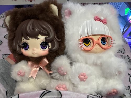 Customer's two Baby Cat Romantic Escape plush toys sitting together. One is fluffy white with glasses and the other has a brown hood.