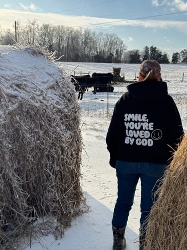 Customer from behind wearing the black Loved by God Oversized Hoodie in a snowy field with hay bales.