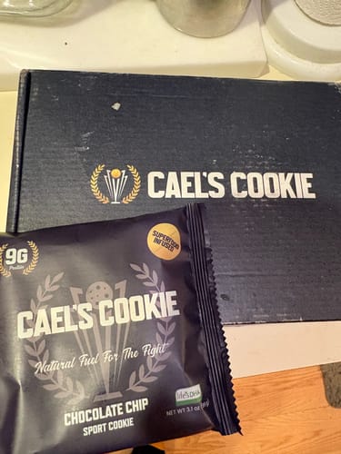 Customer's Cael's Cookie in its wrapper, shown in front of the product box.