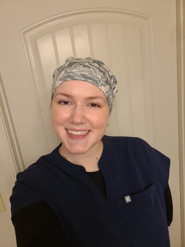 Customer smiling while wearing the DuoStyle Scrub Hat in the Olive Leaves pattern with a navy scrub top.