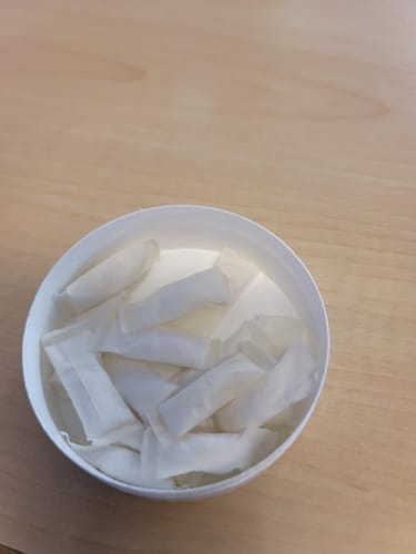 Customer's open container filled with white Refreshing Chill Nicotine Pouches on a wooden table.