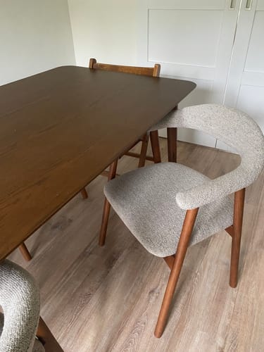 Recensent toont de stijlvolle Nordic eetkamerstoel met greige bekleding en walnoot frame aan een eettafel.