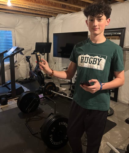 Customer holding a packet of SuperCharged Honey in a home gym with weight equipment in the background.