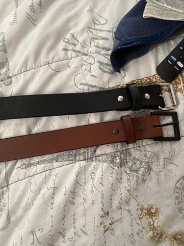 A reviewer's black and brown Gunner belts are laid out side-by-side on a patterned comforter.