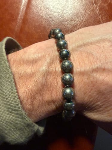 A customer's wrist wearing the pyrite bracelet with uniform, dark beads, against a brown background.