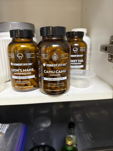 Reviewer's bottle of Camu Camu Berry Capsules on a white shelf inside a cabinet, next to other supplements.