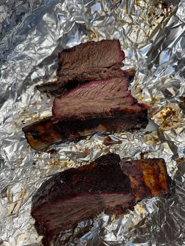 Customer's smoked Bone-In Short Ribs on foil, with one cut to show the tender meat and pink smoke ring.