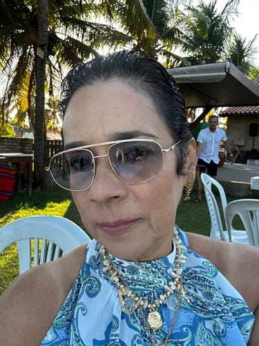Cliente usando os Óculos Aurelia com armação dourada elegante em uma área externa.