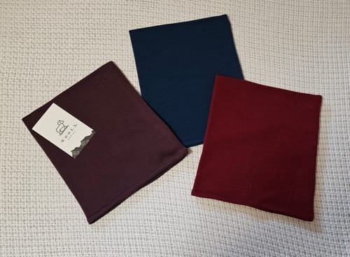 Reviewer's three folded Neck Gaiters, including the rhubarb one, laid out on a textured surface.