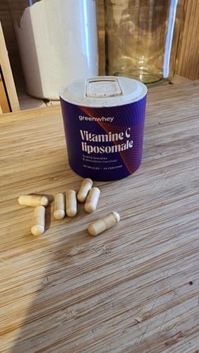Pot de Vitamine C liposomale d'un client avec quelques gélules posées sur une table en bois.