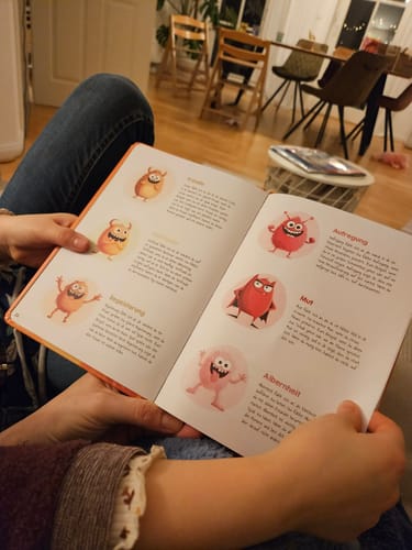 Eine Person hält das aufgeschlagene Gefühlstagebuch für Kinder und zeigt die bunten Illustrationen von Gefühlsmonstern.
