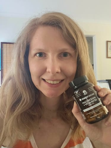 A happy customer smiling while holding a bottle of Magnesium + Vitamin D2.