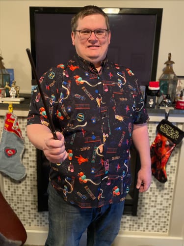 Customer wearing the fun Weasleys’ Wizard Wheezes shirt while holding a wand in front of a festive fireplace.