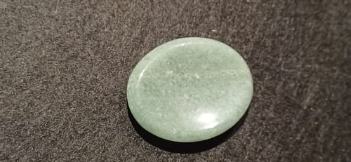 Photo d'un client de la pierre anti-stress Aventurine lisse et verte, posée sur une surface sombre.