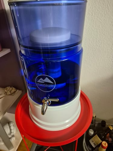 Kundenfoto zeigt den dunkelblauen MAUNAWAI PI®PRIME Glasbehälter, montiert und mit Wasser gefüllt auf seinem weißen Sockel.