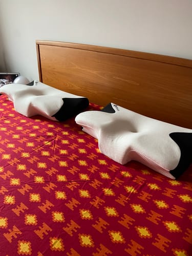 Un client montre deux Coussins d’Alignement Cervical Cellsius blancs et noirs posés sur un lit.
