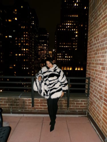 Customer wearing the voluminous Faux Fur Zebra Coat on a balcony with a city view.