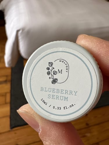 Customer's hand holding the lid of the small, 10ml trial-size Blueberry Serum.
