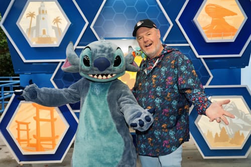 Reviewer in a 'Space Rangers' patterned hoodie, smiling while posing with the character Stitch at a park.