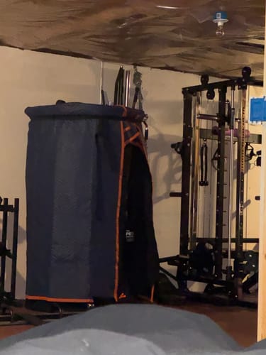 Customer's Sauna Pod 2.0 covered with blue packing blankets in a basement gym.