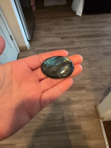 Reviewer's hand holding a polished labradorite palm stone showing a vibrant blue and green flash.