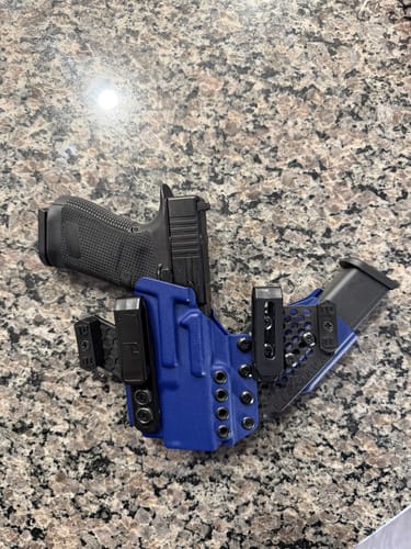 Reviewer's blue APX holster holding a handgun, with the flexible magazine carrier angled on a countertop.