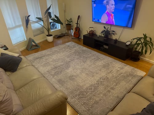 Customer's large Mellow Mat in Silver Mist covering the floor of a cozy living room in front of a sofa.
