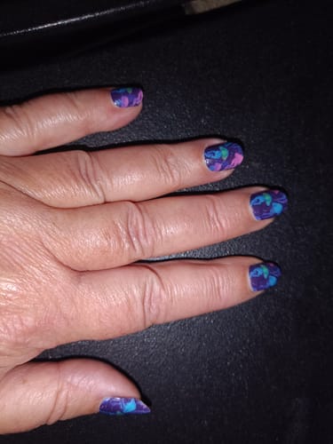 Hand einer Kundin, die die 10 Tage alten Stinging Beauty Nagelfolien mit einem farbenfrohen Design trägt.