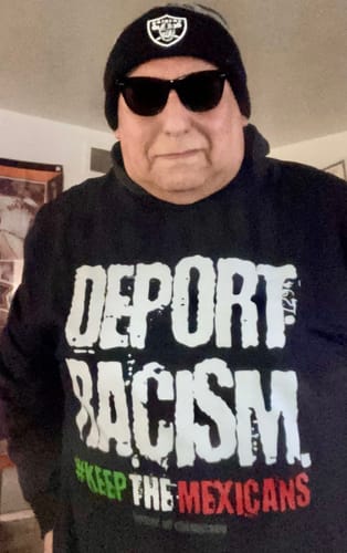 Reviewer wearing the black LA STREETS Deport Racism T-Shirt indoors with a beanie and sunglasses.