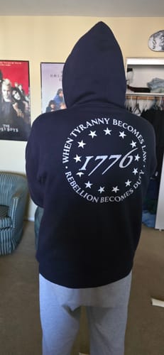 Reviewer showing the back of the black "When Tyranny Becomes Law 1776" hoodie with the hood up.