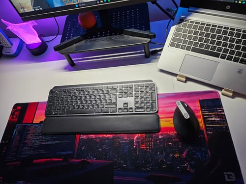 Customer's Sunset Coding desk mat with a colorful cityscape design, shown on a desk with a keyboard and mouse.