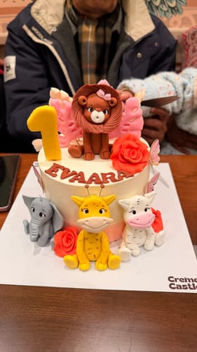 Reviewer's Jungle Lion Kids Cake for a first birthday. The white cake has a cute lion topper and other animal figurines.