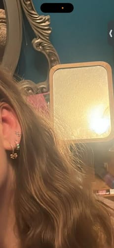 Close-up of a reviewer's ear, showing the gold Colourful Love Earrings in the lobe, with other small earrings higher up.
