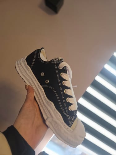 Reviewer houdt de zwarte Maison Mihara Yasuhiro sneaker vast, en toont de opvallende, golvende witte zool.