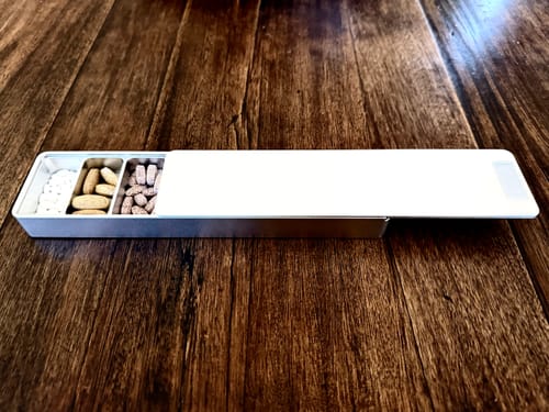 Customer's open aluminum Weekly Case on a wood surface, showing compartments filled with various vitamins.