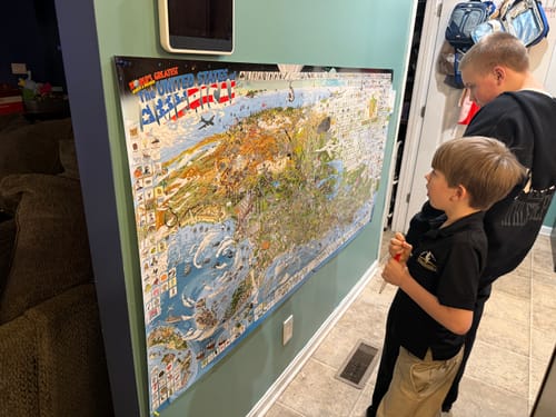 Reviewer and a child looking at the large World's Greatest Search & Discover poster mounted on a green wall.