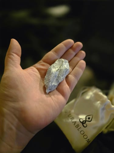 Customer holding a light blue, rough crystal from their AuraBloom Subscription Box, with the branded pouch visible.