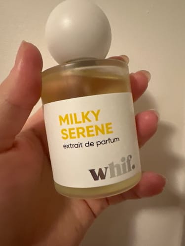 Customer's hand holding a small glass bottle of Milky Serene extrait de parfum.