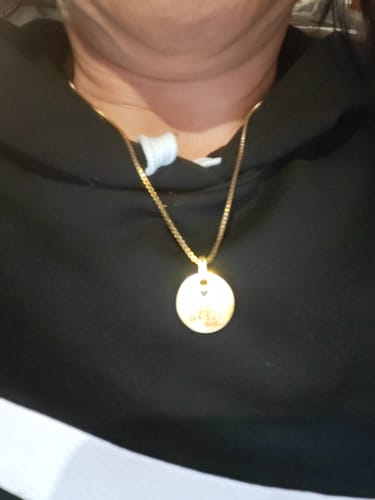 A customer wears the gold-colored Legacy pendant on a chain, shown close-up against their black hoodie.