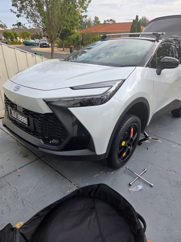 Customer's black spare wheel with a yellow center fitted onto a white car in a driveway.
